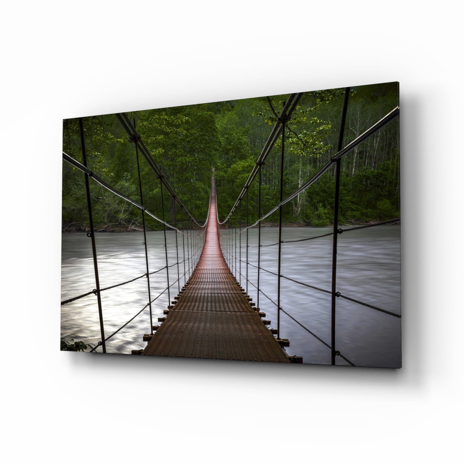 Suspension bridge with red deck stretching over flowing river surrounded by dense green forest canopy.