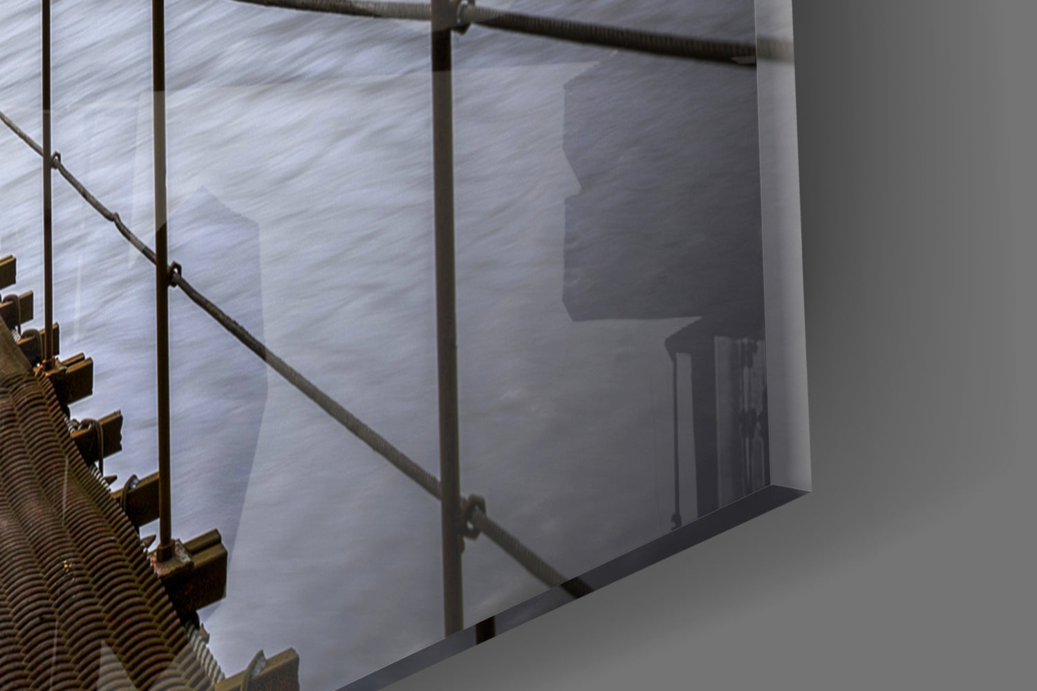 Close-up detail of brass cable clamps and metal railing against frosted glass panel with bridge tower silhouette.