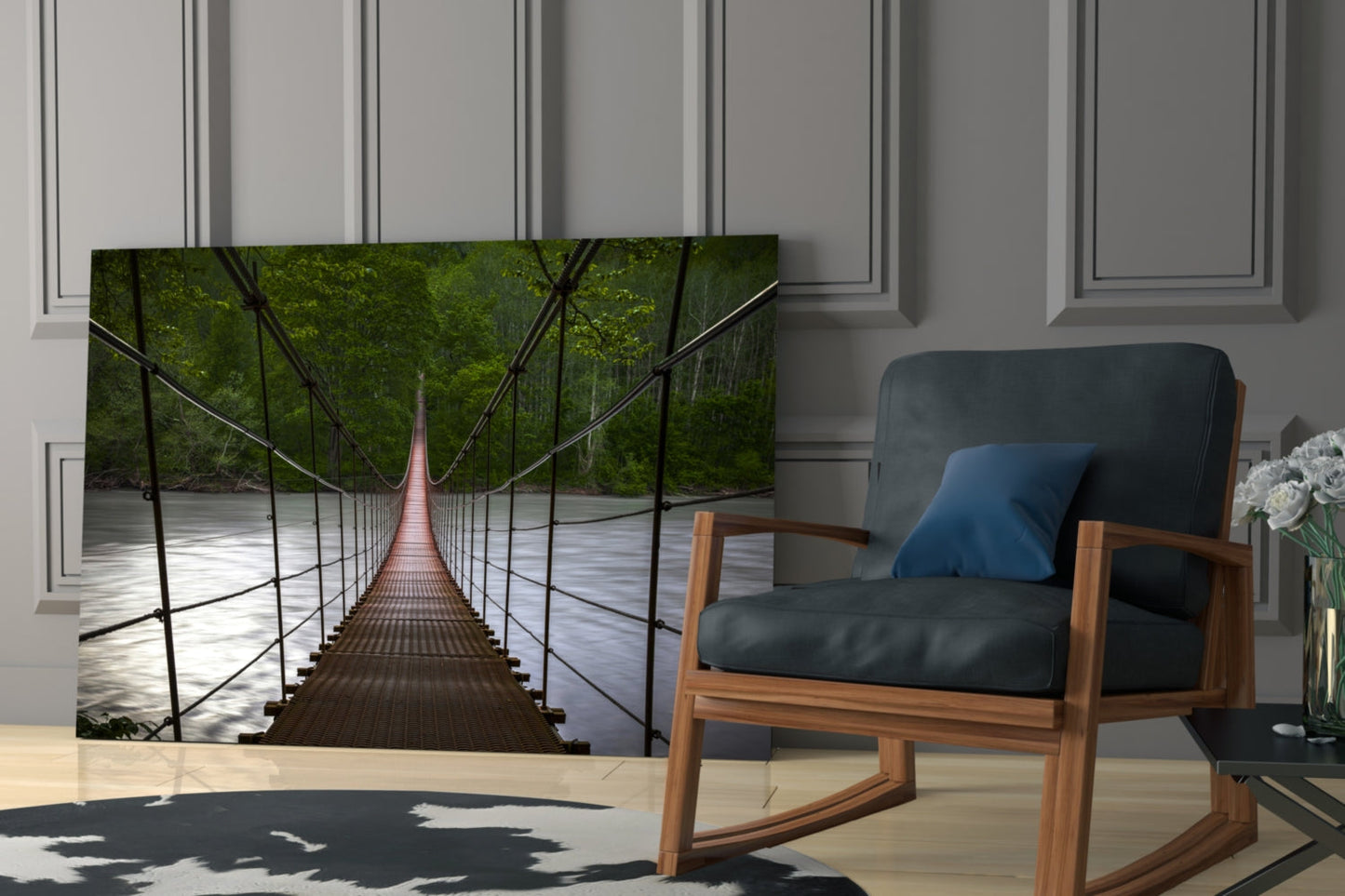 Suspension bridge glass wall art displayed in modern living room beside wooden chair with blue cushion, showing forest canopy and river perspective.
