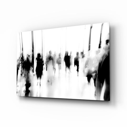 Black and white glass wall art depicting blurred silhouettes of multiple people in an indoor space, displayed at an angle.