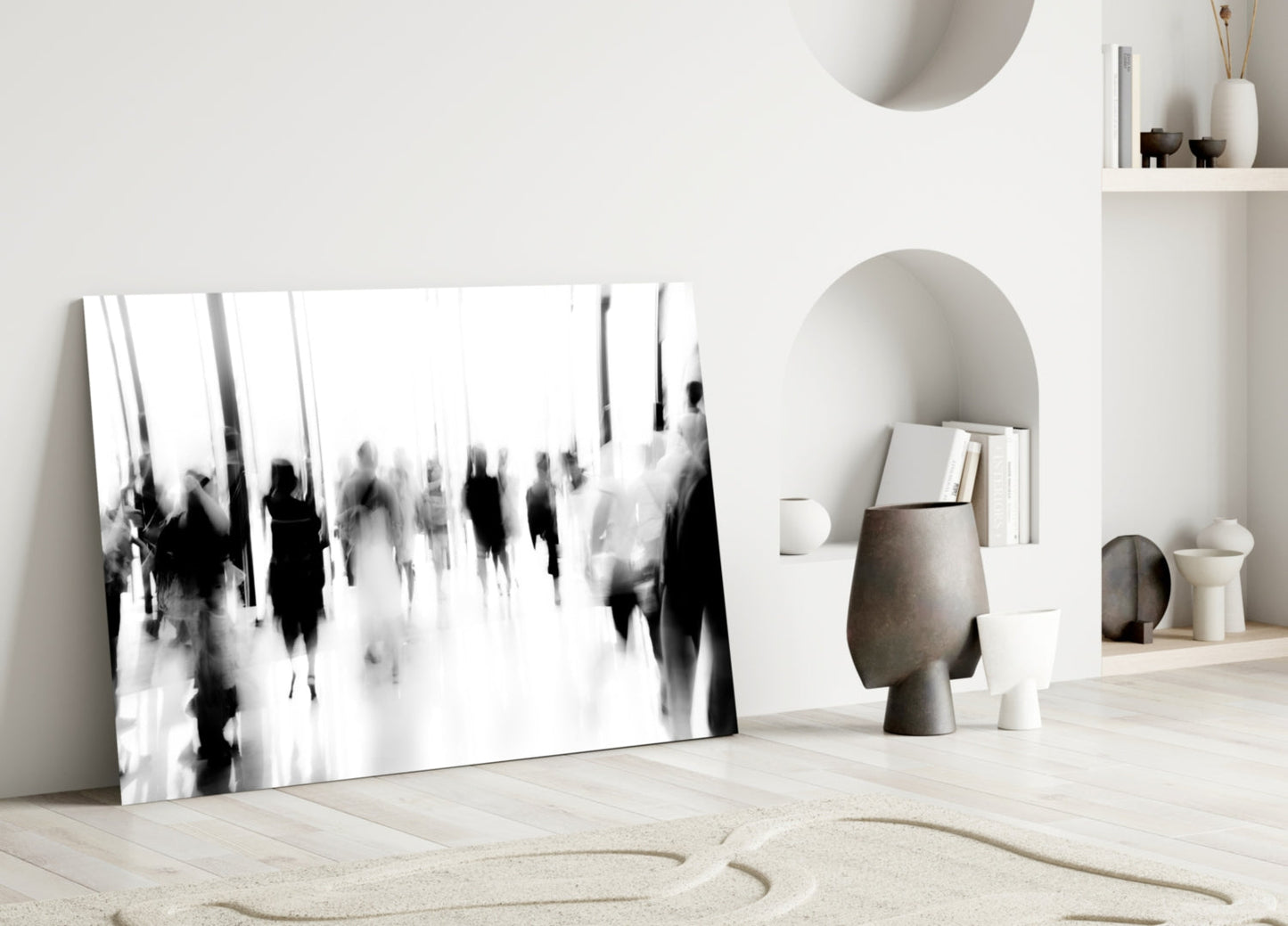 Black and white blurred crowd photograph displayed as glass wall art leaning against white wall in minimalist interior setting.