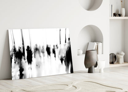 Black and white blurred crowd photograph displayed as glass wall art leaning against white wall in minimalist interior setting.