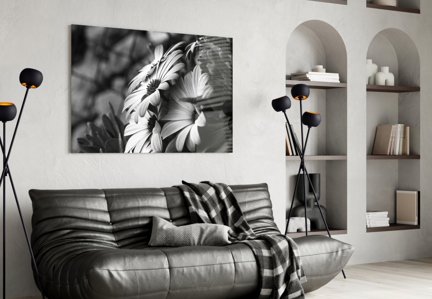 Black and white glass wall art of daisies displayed above a gray leather sofa in a modern living room setting.