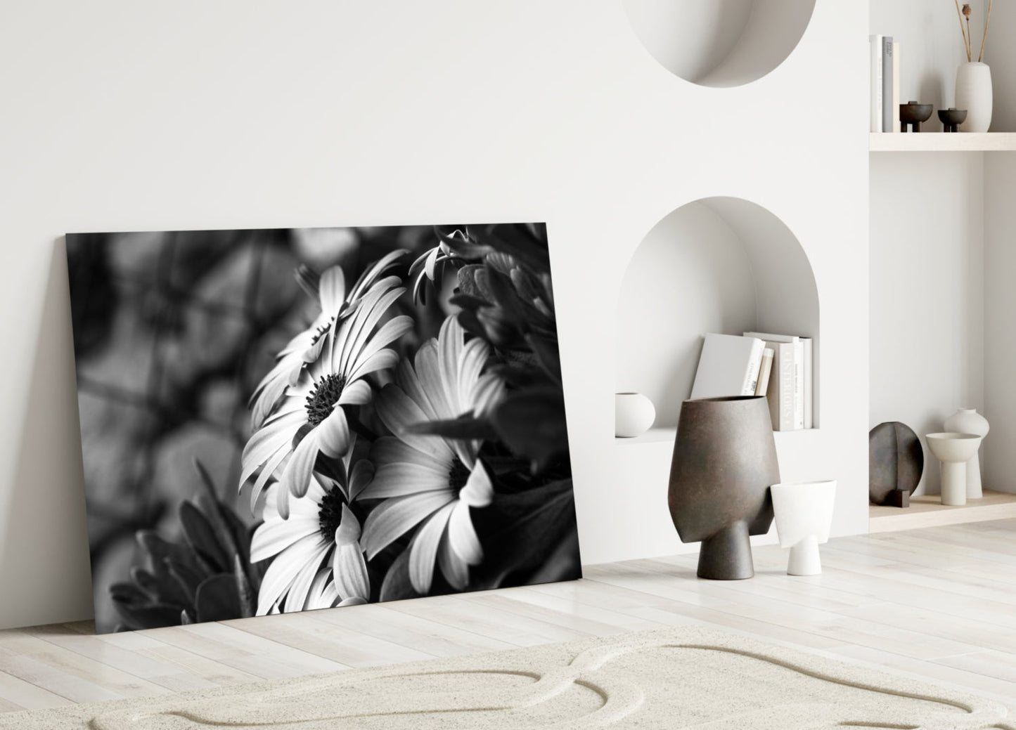 Black and white glass wall art leaning against white wall displays close-up daisy flowers with detailed petals and centers.