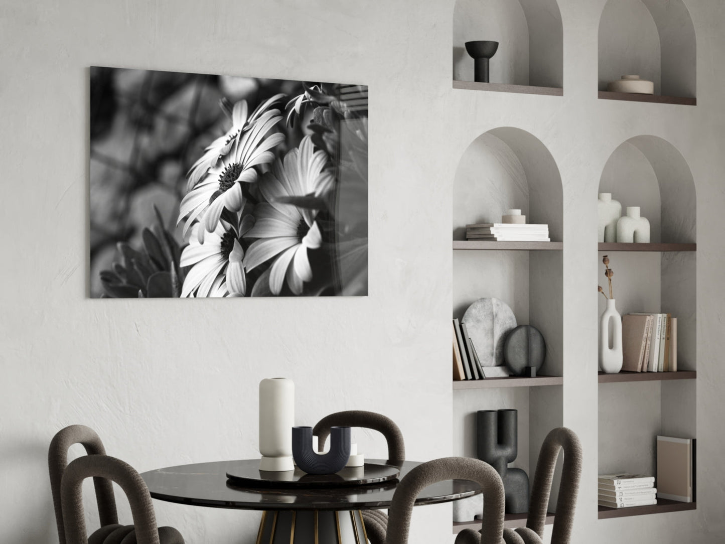 Black and white glass wall art featuring close-up daisy flowers displayed above a round dining table in a minimalist interior.