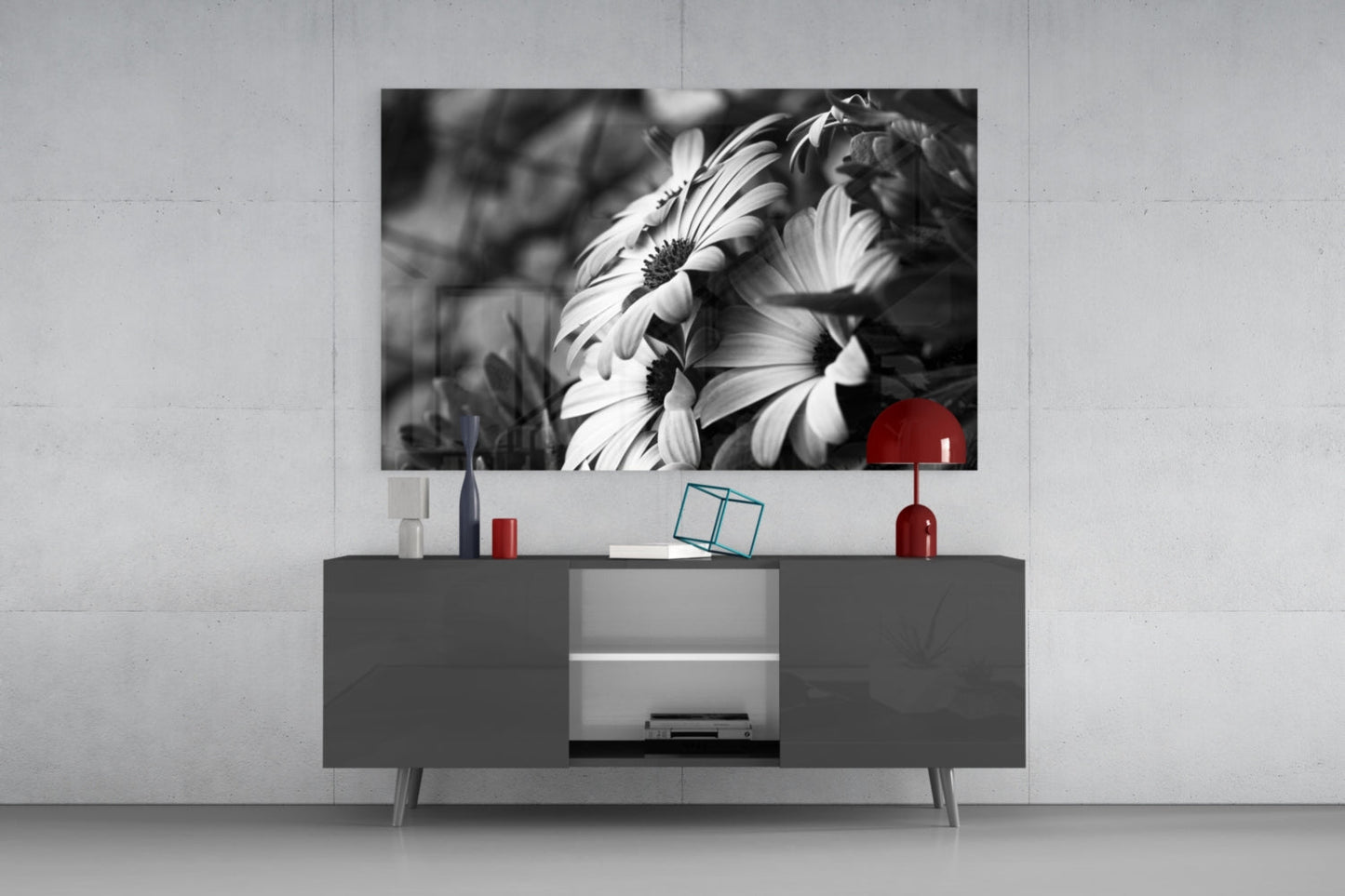 Black and white daisy flowers with red accent displayed on wall above gray media console in modern living room setting.