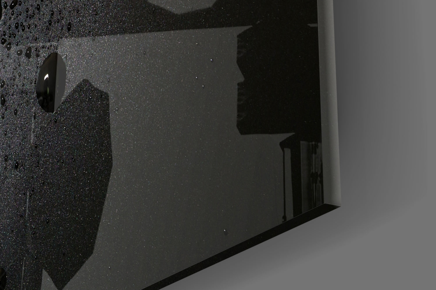 Close-up angled view of black speckled glass wall art with glossy surface and mounting hardware visible.