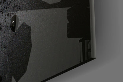 Close-up angled view of black speckled glass wall art with glossy surface and mounting hardware visible.