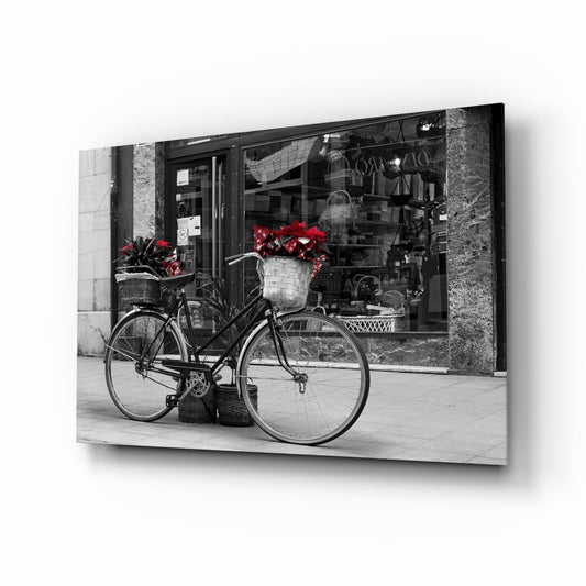 Black vintage bicycle with red flowers in wicker basket parked against storefront, displayed as angled canvas wall art.