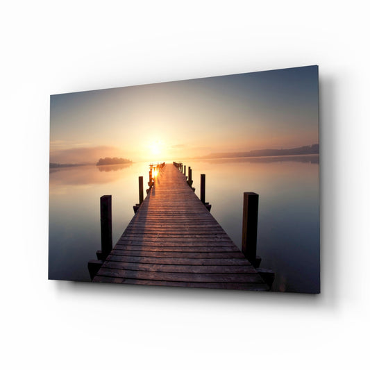 Wooden jetty extending toward a golden sunrise over still water, displayed as a mounted glass wall panel with shadow effect.