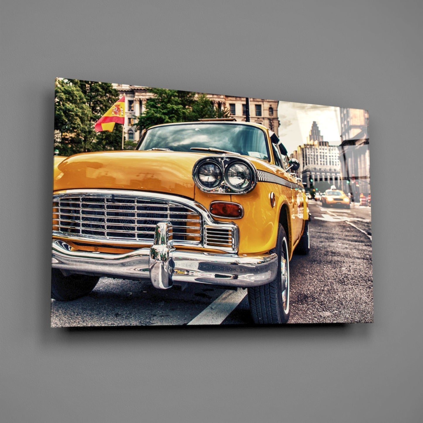 Yellow vintage taxi cab with chrome details parked on street with Spanish flag and city buildings visible in background.