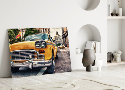 Classic yellow taxi glass wall art leaning against white wall in minimalist room setting with decorative objects.