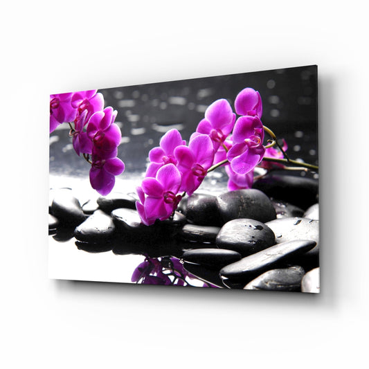 Angled view of glass wall art featuring vibrant magenta orchid flowers and dark zen stones on monochromatic background.