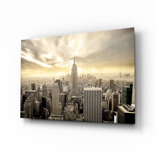 Aerial view of Manhattan skyline featuring Empire State Building centered among skyscrapers under golden cloudy sky, mounted as glass wall art.