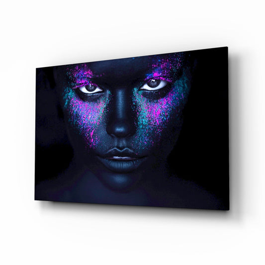 Glass wall art displaying a face with glowing magenta and cyan powder effects around the eyes against a dark background.
