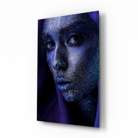 Angled perspective of a glass wall art panel displaying a face covered in silver glitter against a dark blue and purple gradient background.