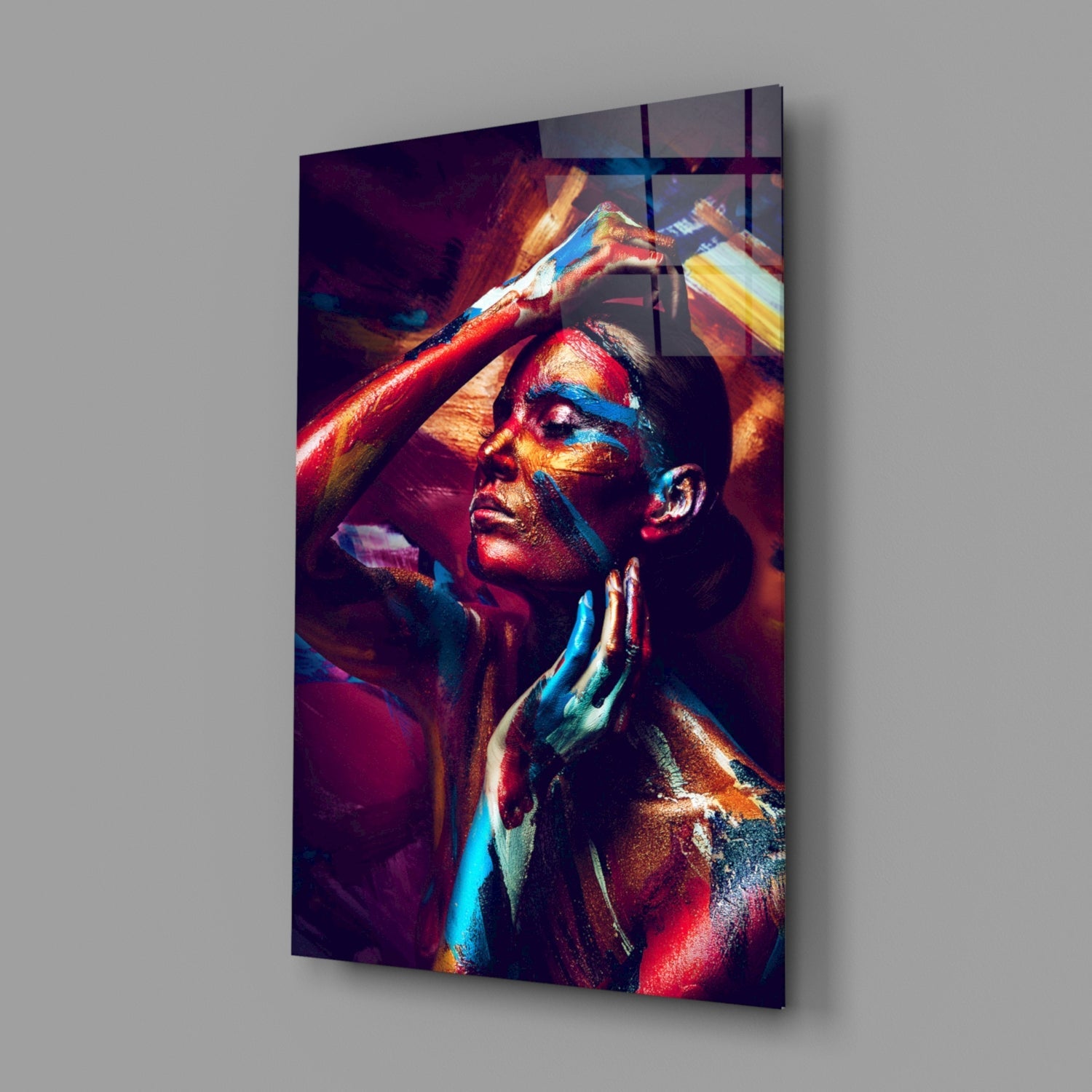 Angled view of a glass wall art depicting a woman with vibrant red, blue, and gold body paint, head tilted back with arms raised.