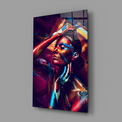 Angled view of a glass wall art depicting a woman with vibrant red, blue, and gold body paint, head tilted back with arms raised.