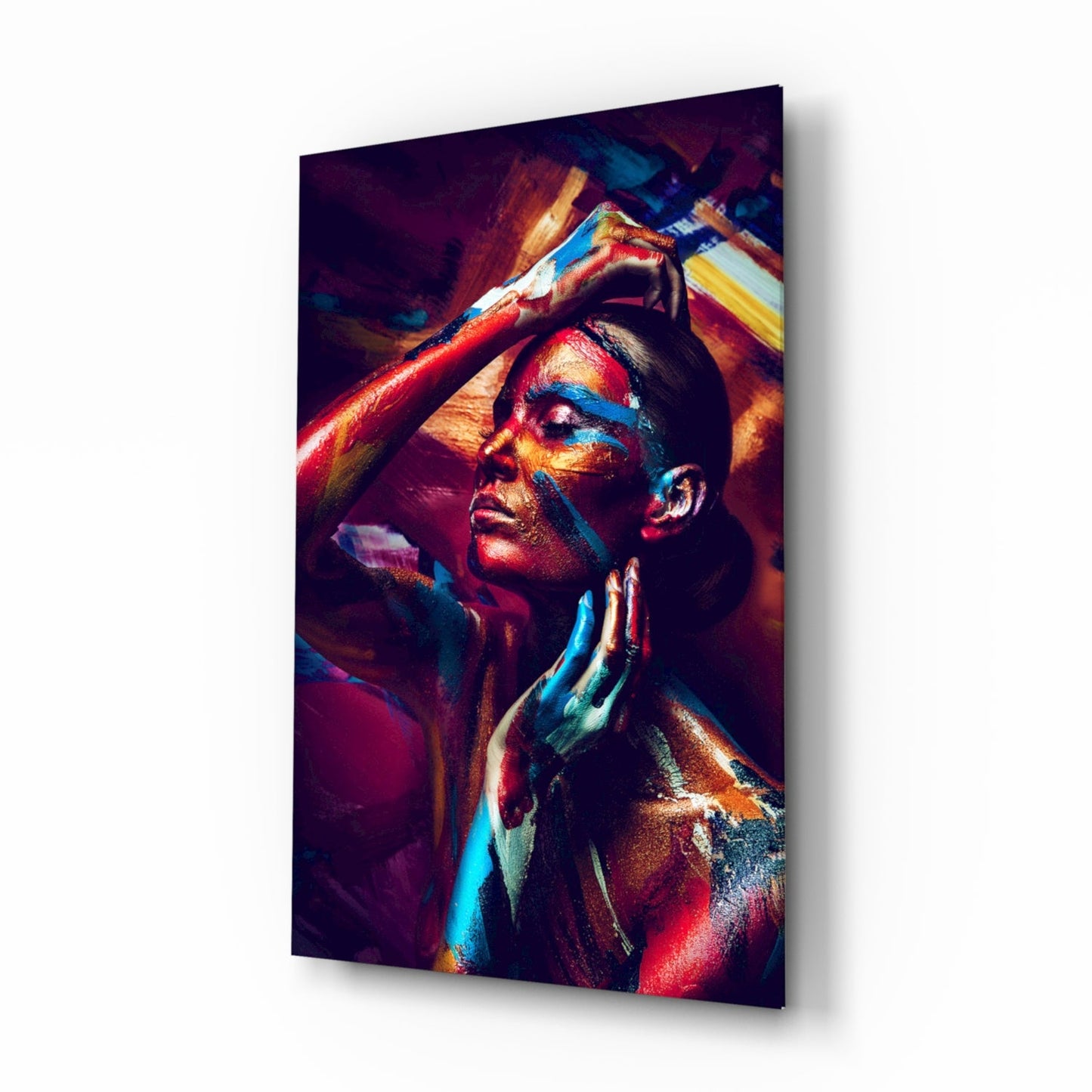 Woman with vibrant blue, red, and gold body paint gazing upward against dark background on glass wall art.
