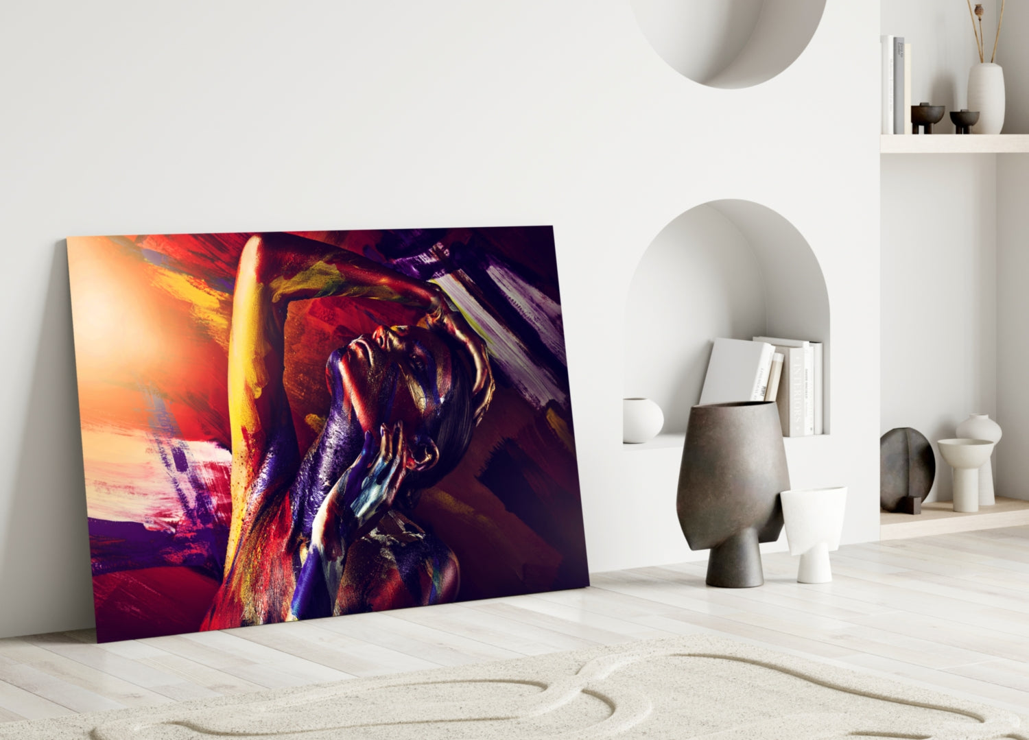 Colorful glass wall art depicting an abstract woman portrait in vibrant reds, golds, and purples, displayed leaning against a white wall in a minimalist interior.