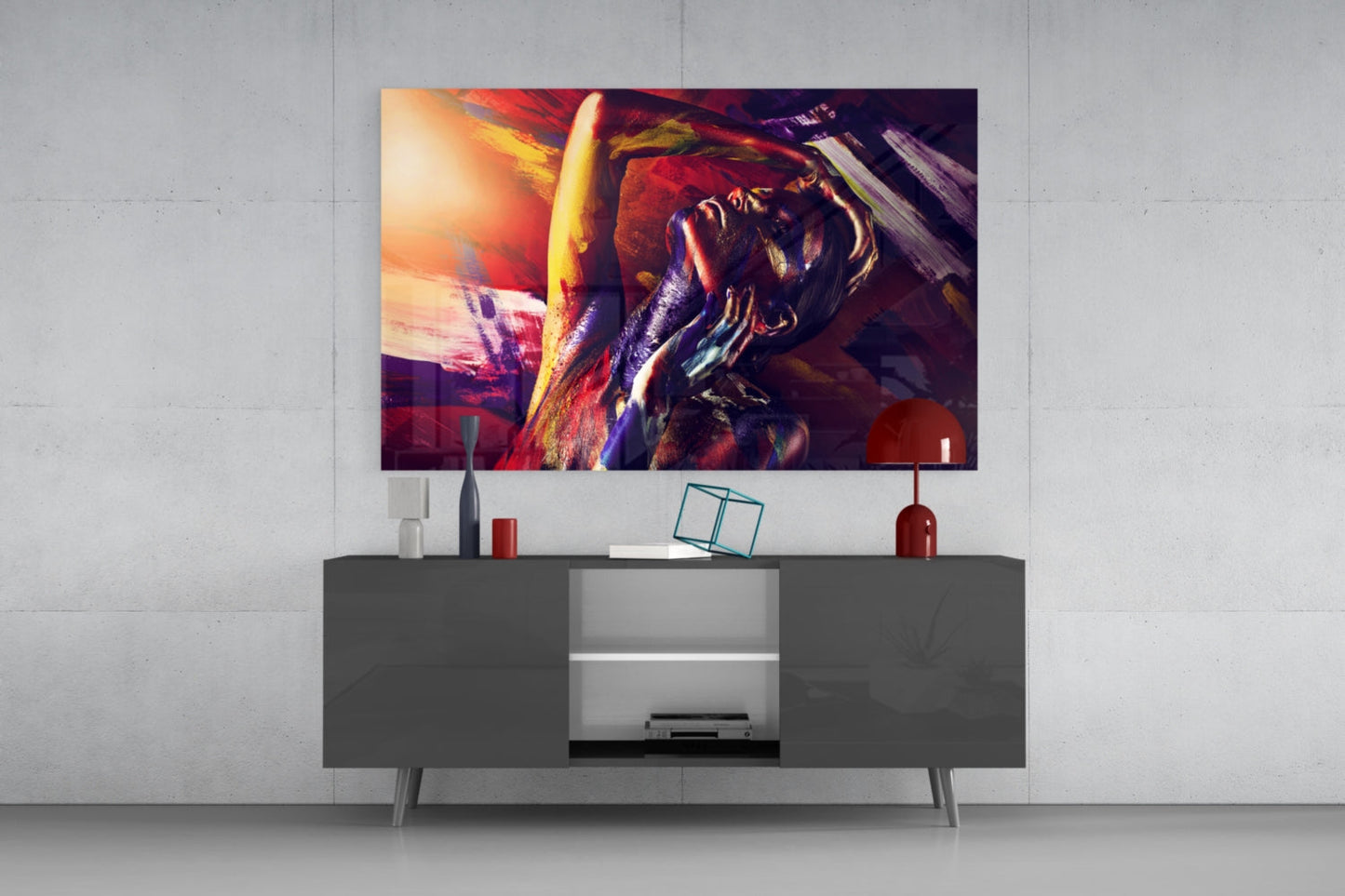 Colorful glass wall art depicting a woman's portrait in vibrant reds, golds, and purples displayed above a dark media console in a modern interior setting.