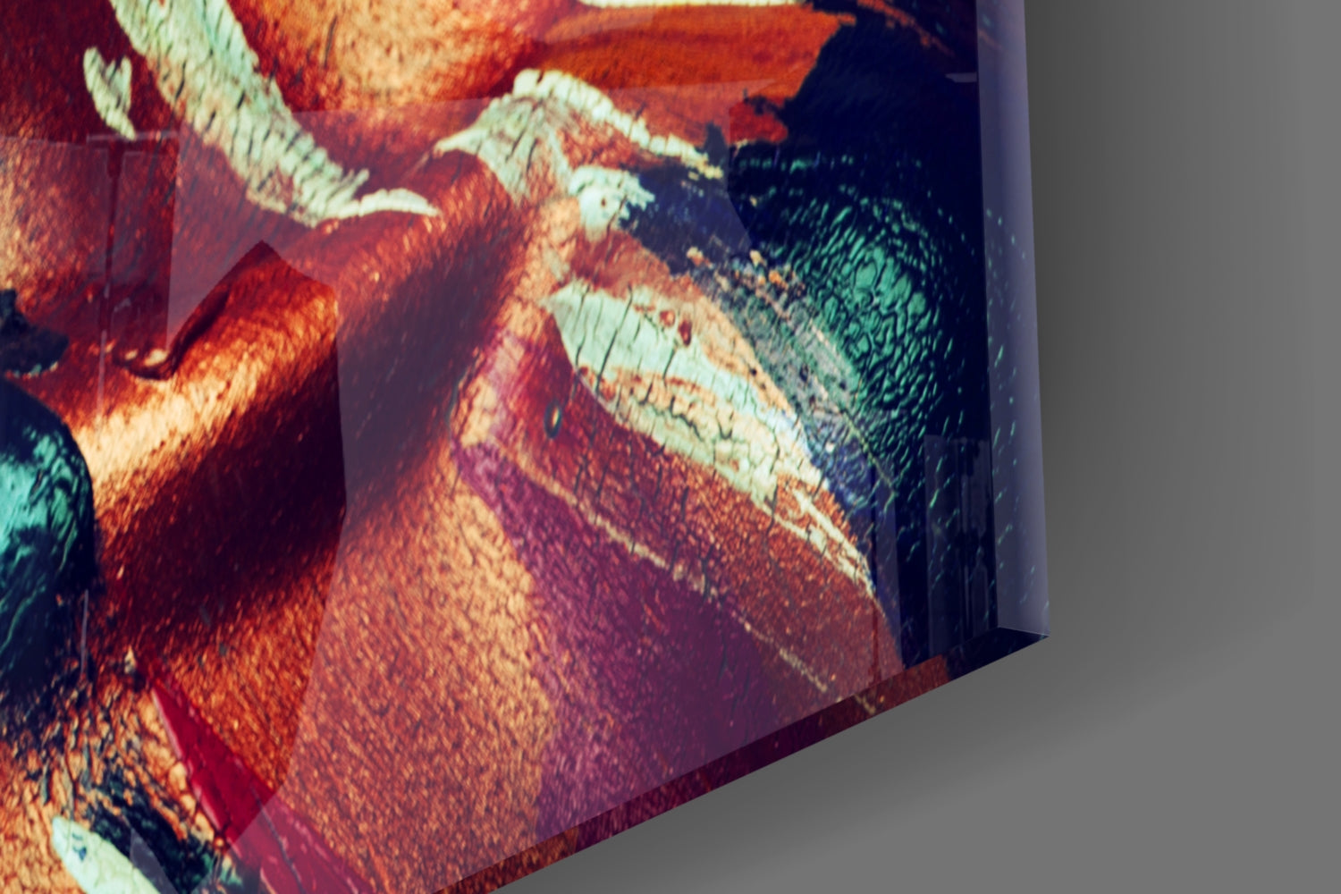Close-up angled view of glass wall art showing vibrant red, orange, cream, and teal colors with textured surface detail and curved edge.