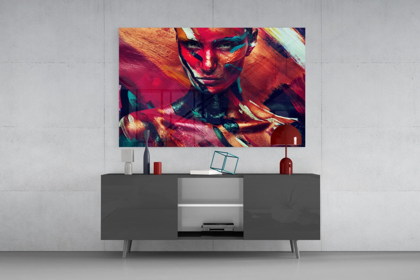 Colorful glass wall art featuring a woman's portrait with red, orange, and teal paint effects displayed above a modern gray media console.