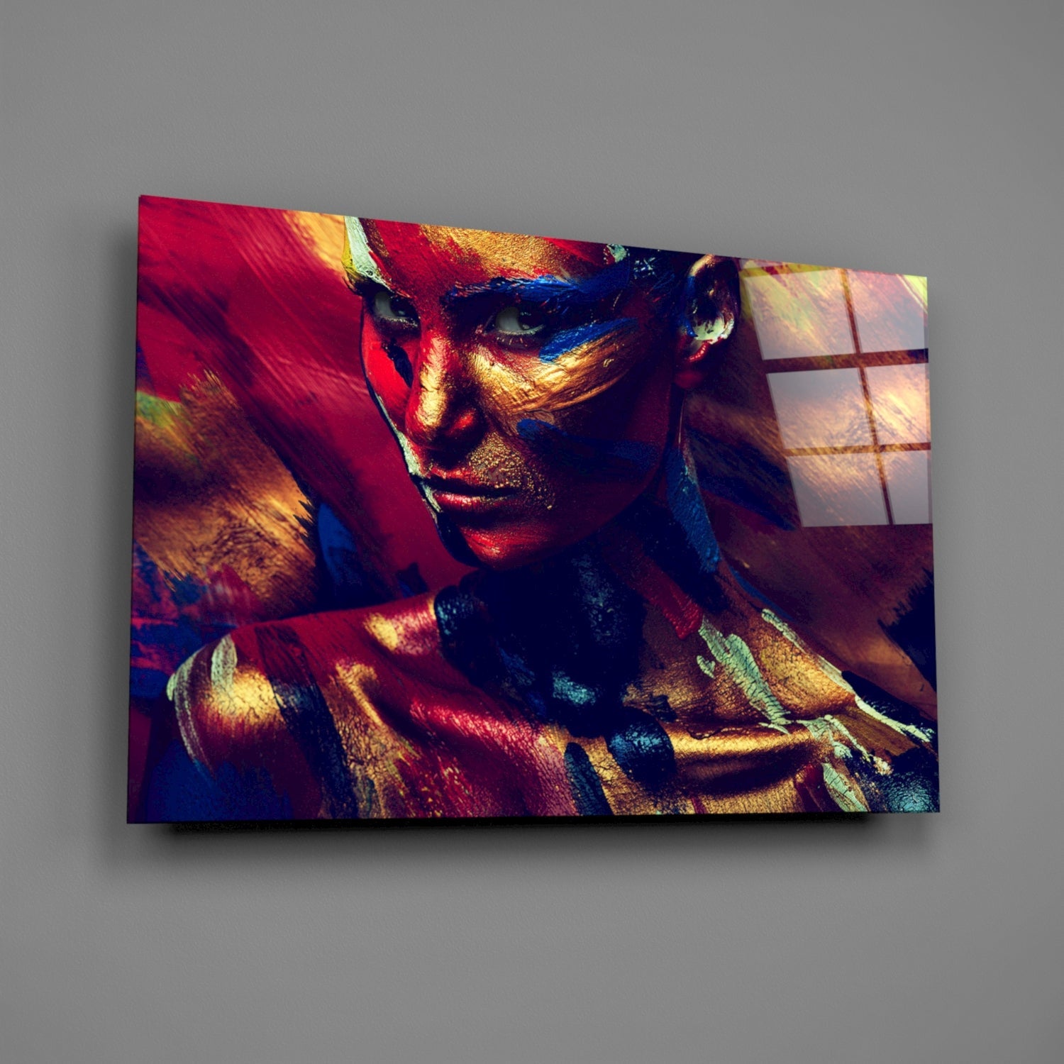 Angled view of glass wall art displaying a woman's face painted in vibrant reds, golds, and blues with geometric patterns.