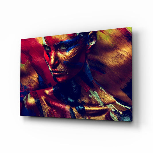 Woman's face and shoulders with vibrant red, gold, and blue body paint against dark background on glass wall art.