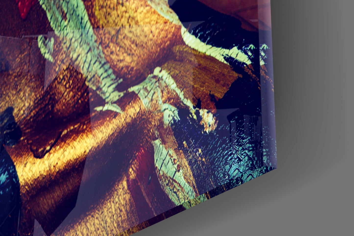 Close-up angled view of glass wall art showing warm yellow, orange, and cool green tones with textured surface detail.