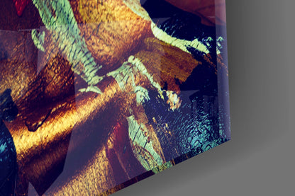 Close-up angled view of glass wall art showing warm yellow, orange, and cool green tones with textured surface detail.