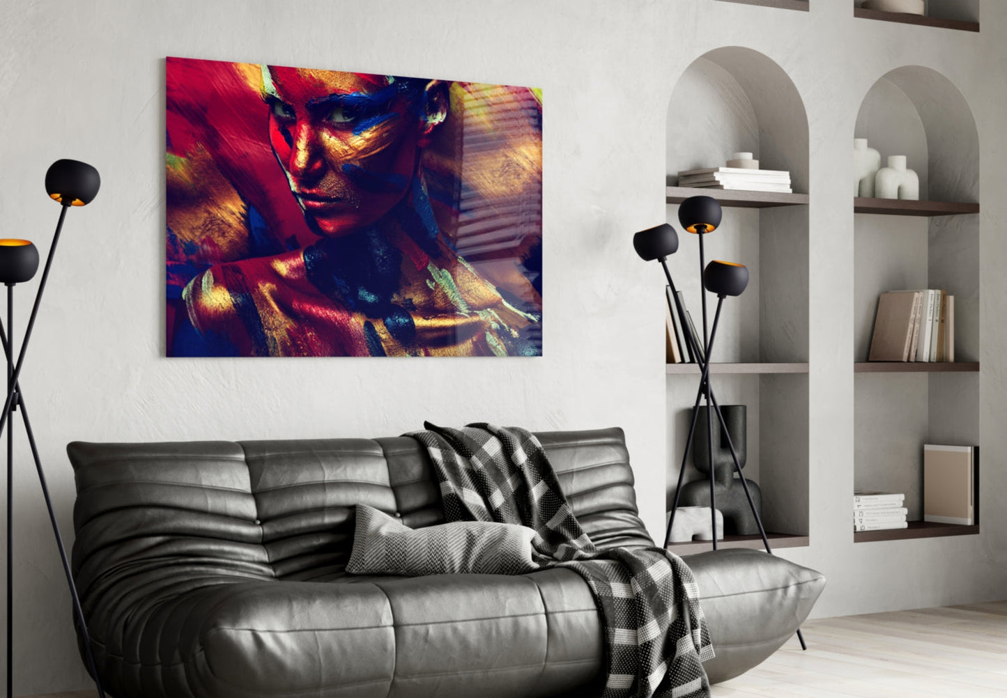Vibrant glass wall art depicting a colorful female portrait with red, gold, and blue tones displayed above a gray leather sofa in a modern living room setting.