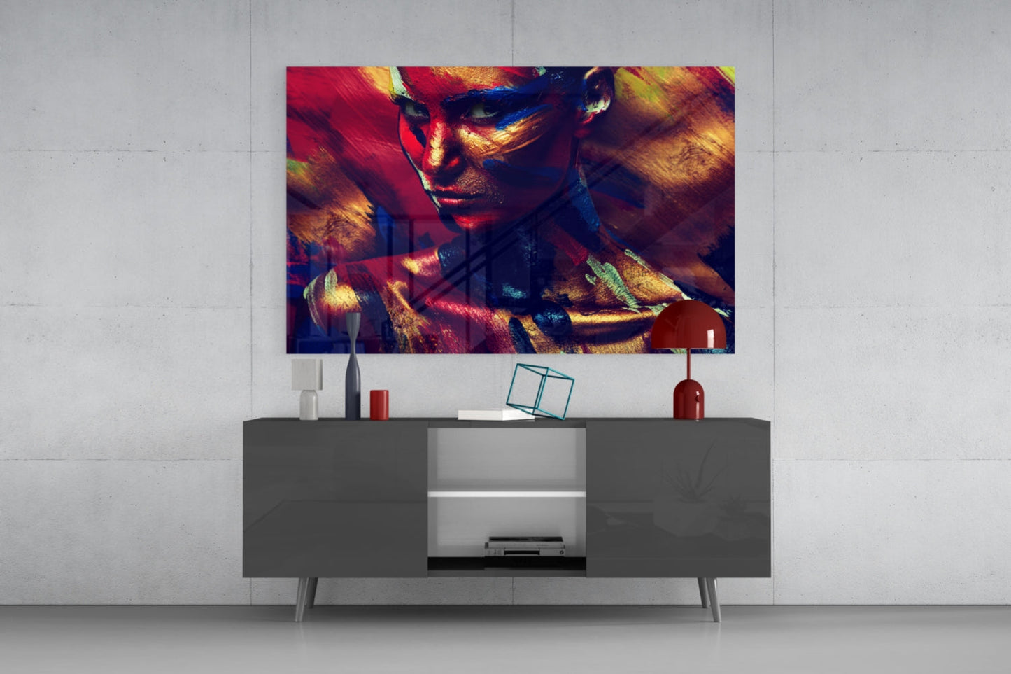 Colorful glass wall art featuring a female portrait with red, gold, and blue paint effects displayed above a dark gray media console in a modern living room setting.