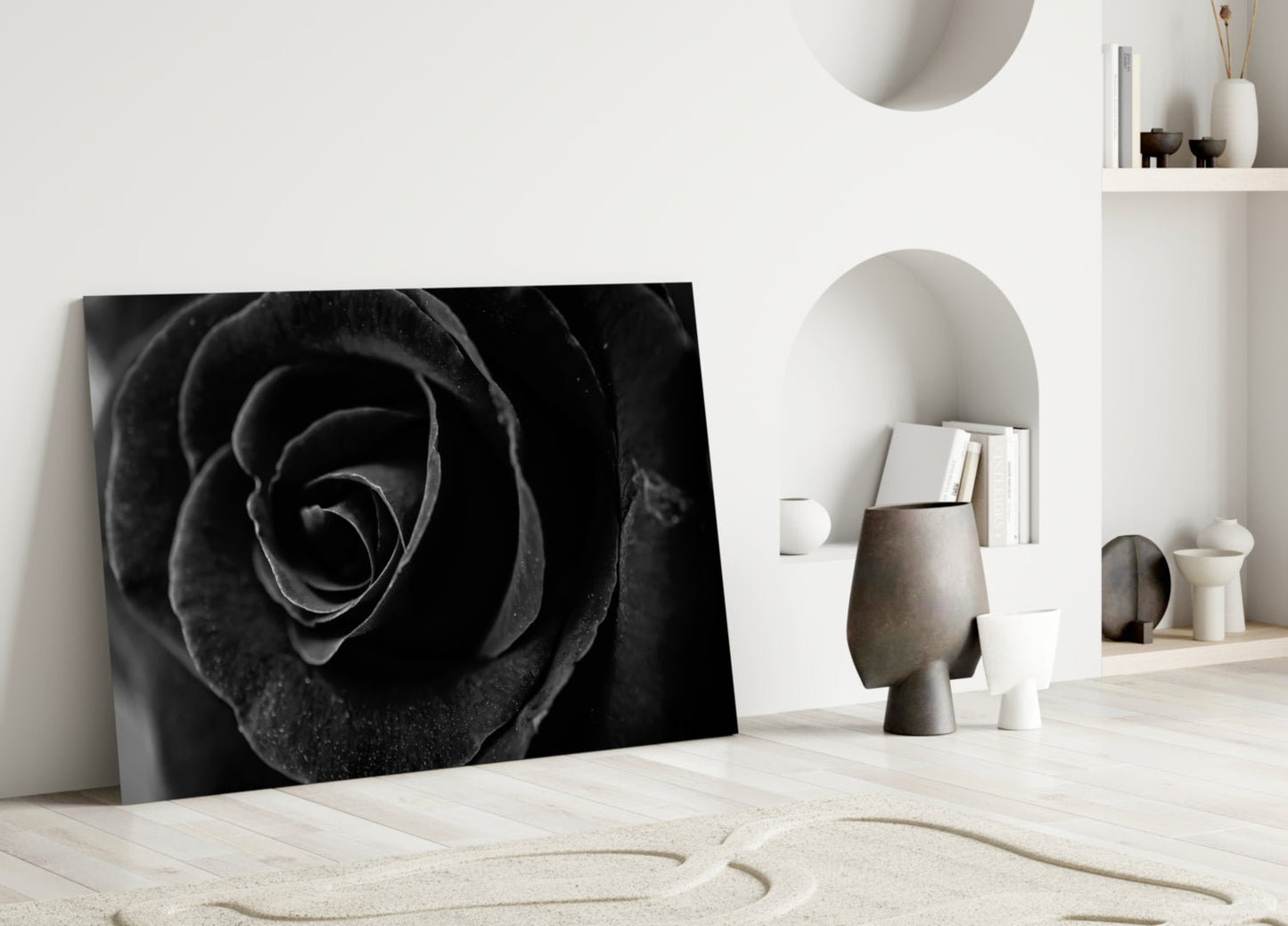 Black rose glass wall art leaning against white wall in minimalist room with decorative objects and shelving.