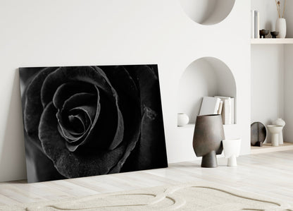Black rose glass wall art leaning against white wall in minimalist room with decorative objects and shelving.