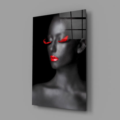 Portrait of woman with red lips and glowing red eyes on black glass panel with grid overlay, displayed at angle against gray wall.