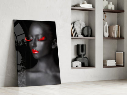 Black and white portrait glass art leaning against white wall with red neon-glowing eyes and lips, displayed beside wooden shelves holding books and decorative objects.