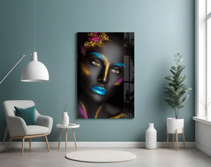 Glass wall art portrait of a woman with black skin, golden and blue face paint, colorful flowers, and vibrant blue lips displayed in a modern living room setting.