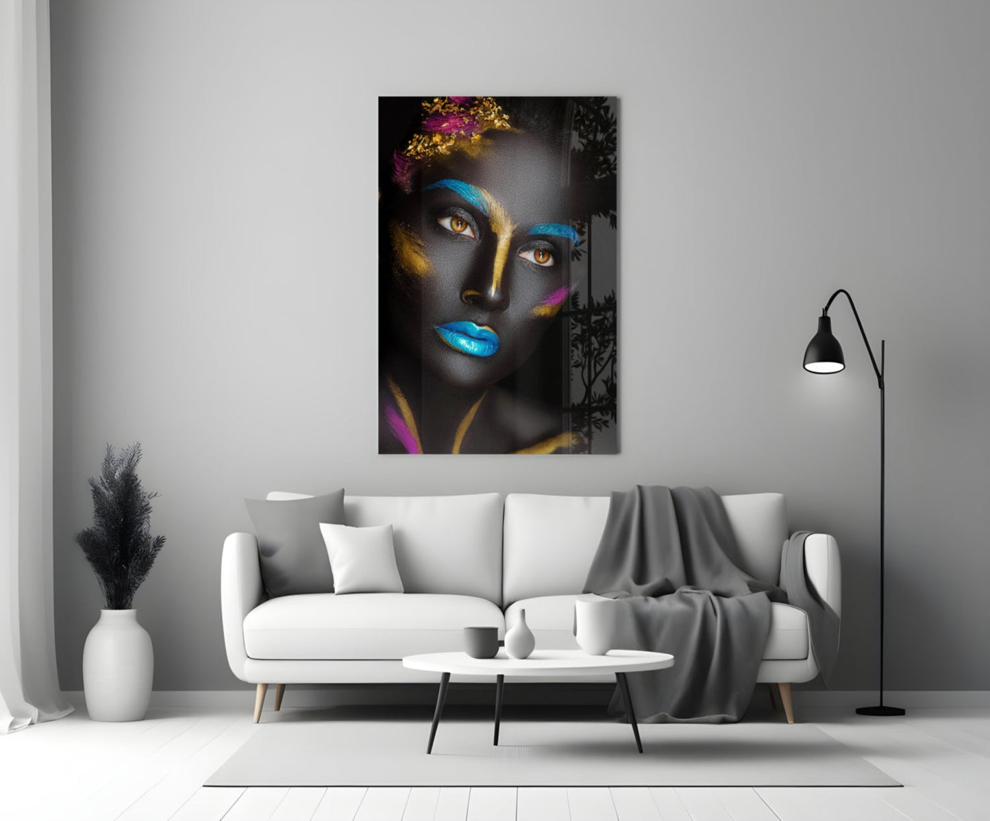 Glass wall art depicting a woman's face with dark skin, blue and gold paint, striking amber eyes, displayed above a white sofa in a modern living room.