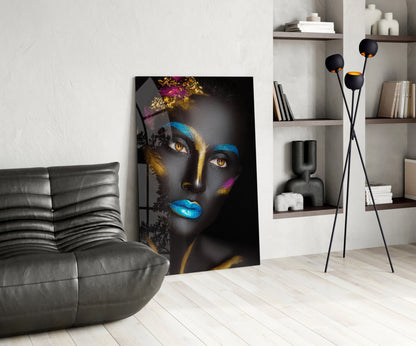 Modern living room interior featuring a glass portrait of a woman with black skin, gold and blue facial paint, displayed against a white wall next to a gray leather chair.