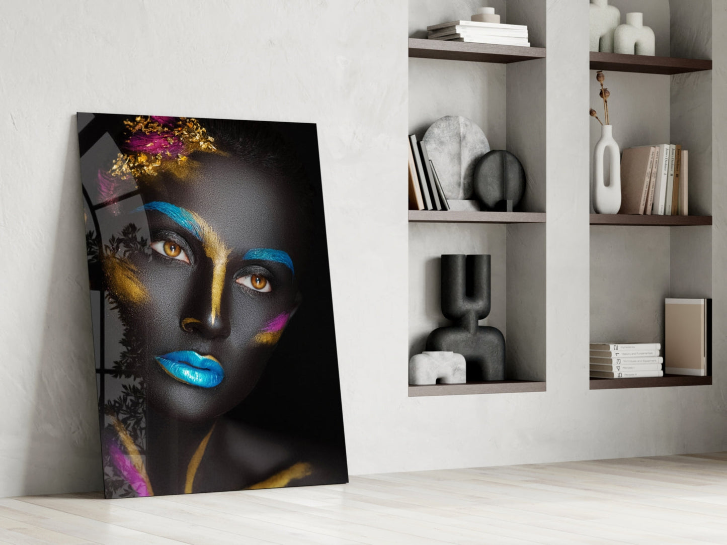 Glass portrait artwork leaning against white wall beside built-in shelving displaying decorative objects and books.