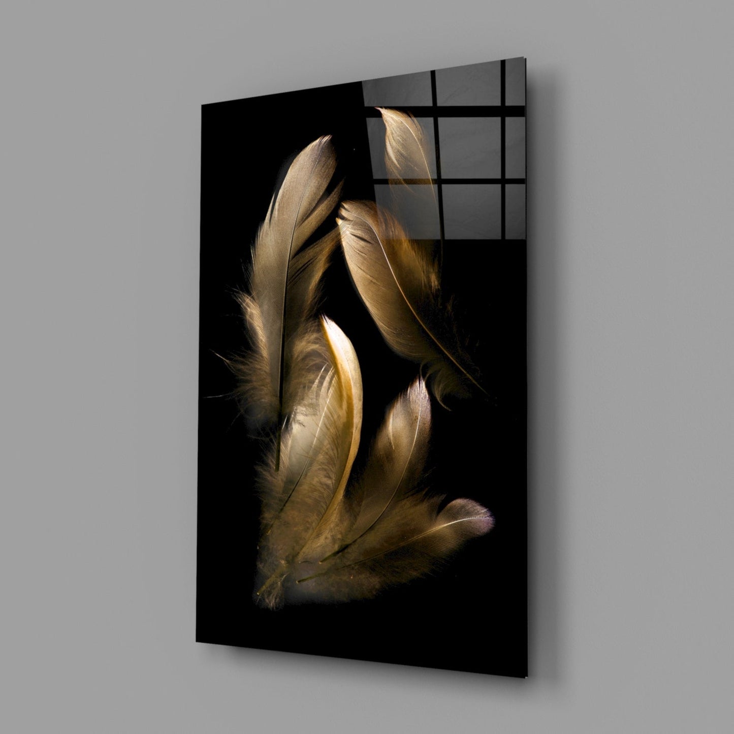 Angled view of black glass wall art featuring golden-brown feathers illuminated against dark background with grid pattern overlay on upper right.