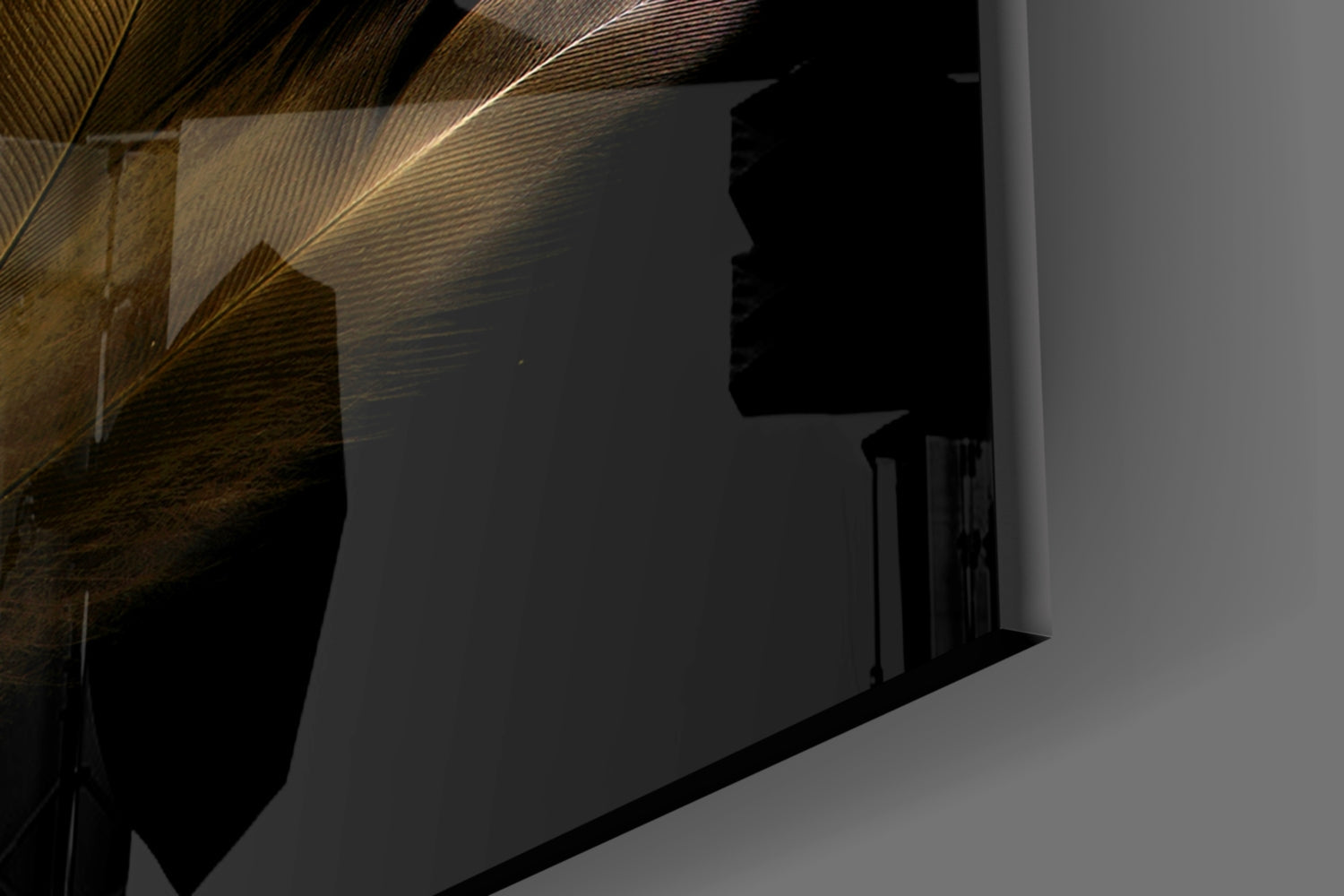 Close-up angled view of tan feather glass wall art mounted on white wall with dramatic lighting and shadows.