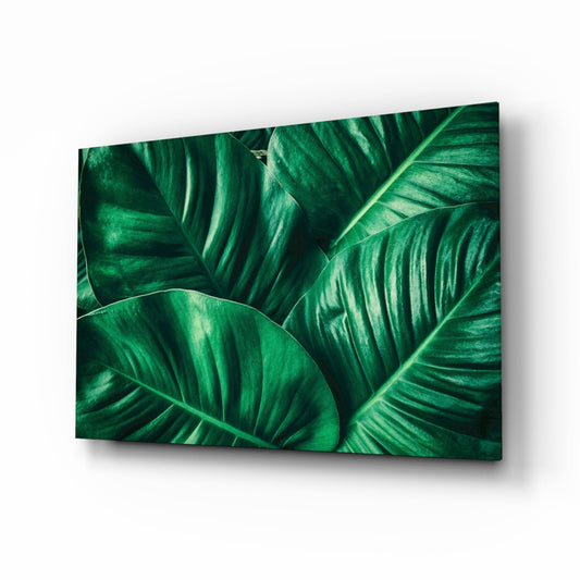 Glass wall art panel displaying close-up tropical leaves with prominent veins in deep and light green tones.