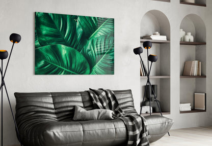 Green tropical leaf glass wall art hung above a gray leather sofa in a modern living room interior.