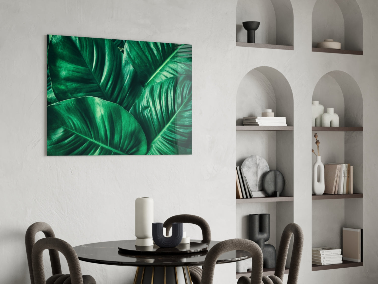 Green tropical leaf glass wall art displaying bold emerald foliage hung above a black dining table in a modern interior space.