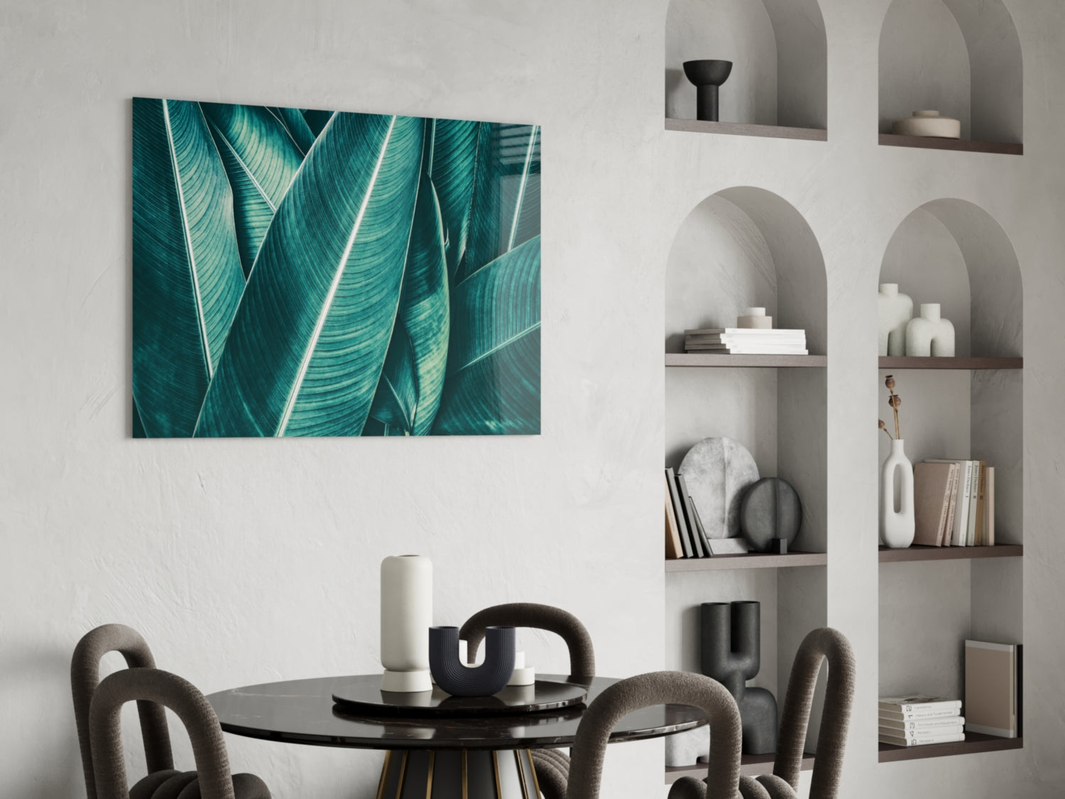 Teal tropical leaf glass wall art displayed above a black dining table in a modern interior with white built-in shelving.