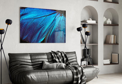 Modern living room with blue butterfly wing glass wall art above black leather sofa, flanked by decorative floor lamp and white shelving.