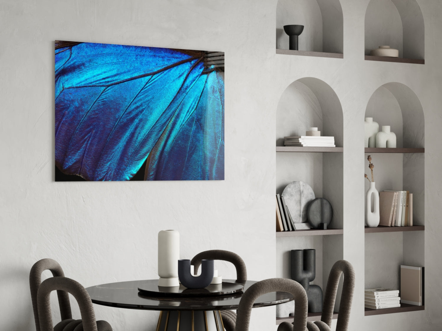 Blue iridescent butterfly wing glass art hanging above a black dining table in a modern room with white built-in shelving.