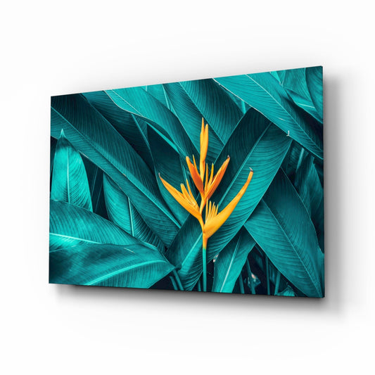 Angled view of glass wall art displaying a vibrant yellow-orange bird of paradise flower amid deep teal tropical leaves.